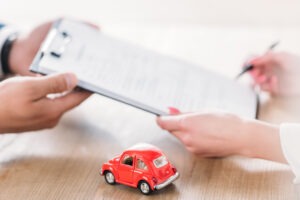 partial view of car dealer giving clipboard to client near miniature car